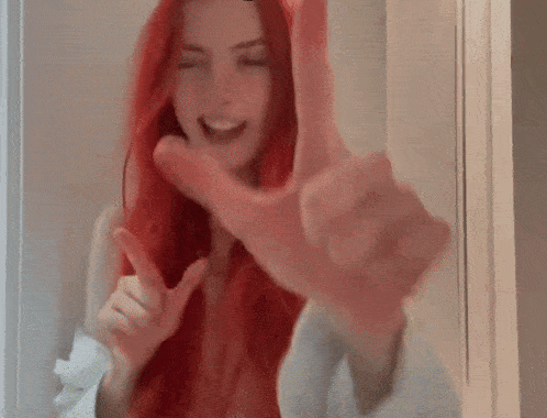 a woman with red hair is making a peace sign with her hands while smiling .