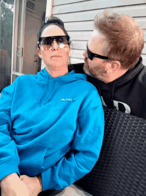a man and a woman are sitting on a couch and the woman is wearing a blue hoodie that says auto