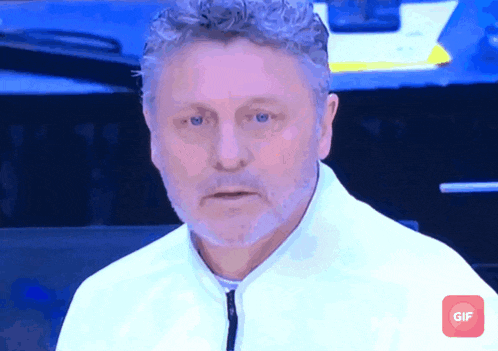 a man with curly hair and a beard looks at the camera with a gif icon next to him