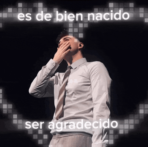 a man in a white shirt and tie is covering his mouth with his hand and the words es de bien nacido ser agradecido are behind him