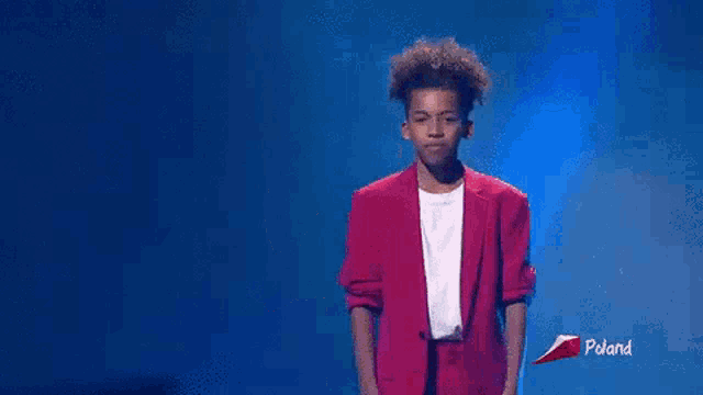 a young man in a pink jacket and white shirt is standing on a stage .