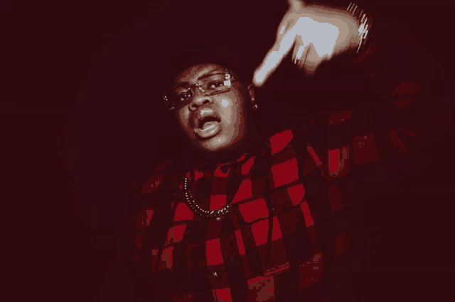 a man wearing glasses and a plaid shirt is making a gesture with his hand
