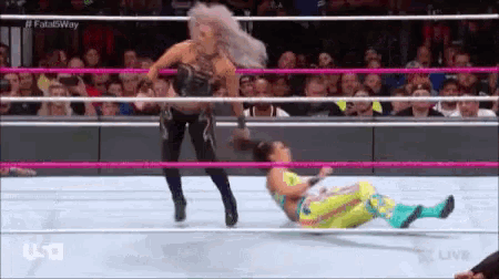 a woman is standing in a wrestling ring with another woman laying on the ground .
