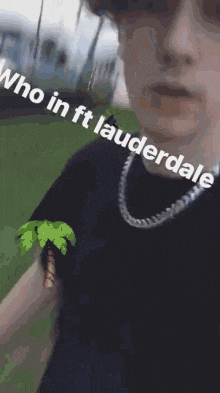 a man wearing sunglasses and a necklace is holding a small palm tree on his arm .