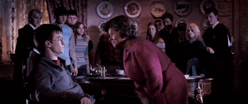 harry potter is sitting in a wheelchair talking to a woman in a room with a group of people .