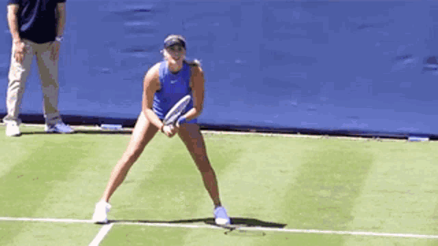 a woman in a blue tank top is holding a tennis racket on a tennis court