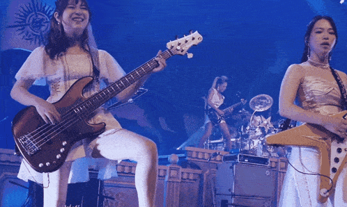 a woman playing a bass guitar while another woman plays drums