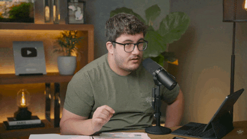 a man wearing glasses and a green shirt is sitting in front of a microphone and a laptop