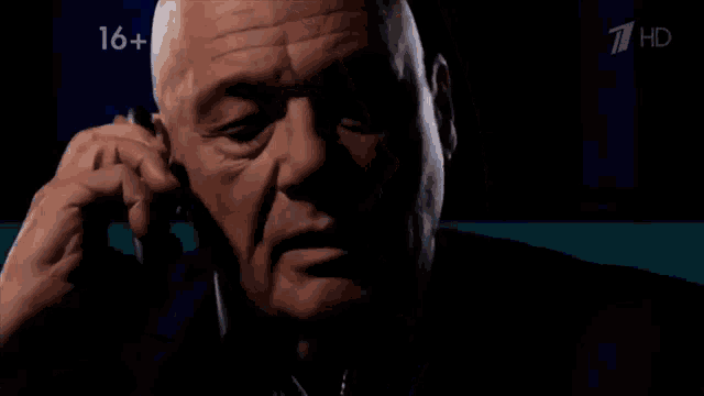 a bald man looking at a cell phone with the number 16+ on the bottom