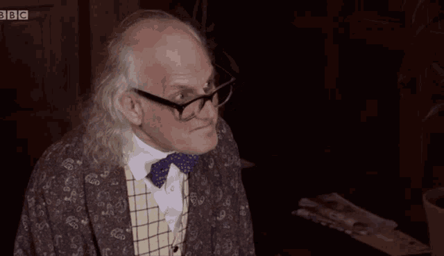 a man wearing glasses and a bow tie has a bbc logo in the background