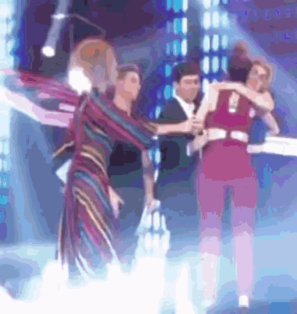 a woman in a red dress is hugging another woman in a striped dress on a stage .