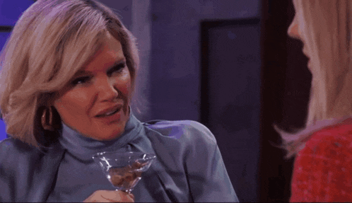 a woman in a blue turtleneck is holding a martini glass and talking to another woman