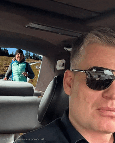 a man wearing sunglasses sits in a car with a woman in the background