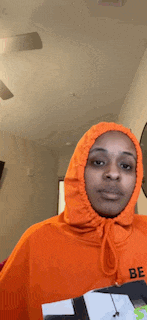 a woman wearing an orange hoodie is giving the peace sign .