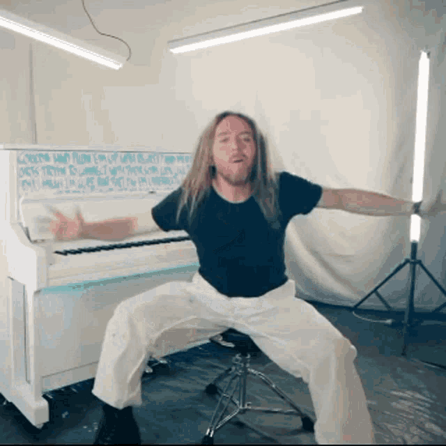 a man is squatting in front of a white piano that has a chalkboard behind it that says " canada "
