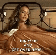 a woman is laying in bed with the words `` hurry up and get over here '' written on it .