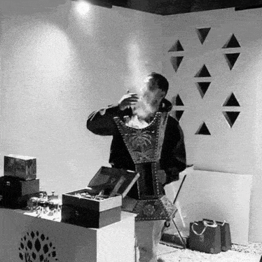 a black and white photo of a man smoking a cigarette in front of a wall with triangles on it