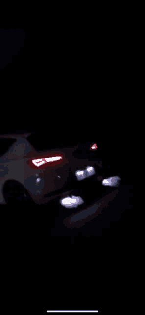 a white car is driving down a dark road at night with its lights on .