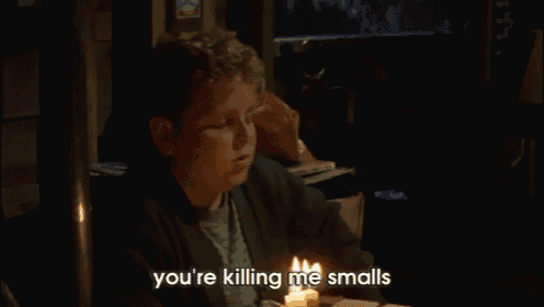 a boy is sitting at a table with a lit candle and says you 're killing me smalls