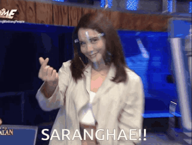 a woman wearing a face shield is making a heart with her fingers and the word saranghae is written below her