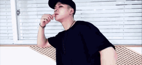a man wearing a black hat and a black t-shirt is licking his lips