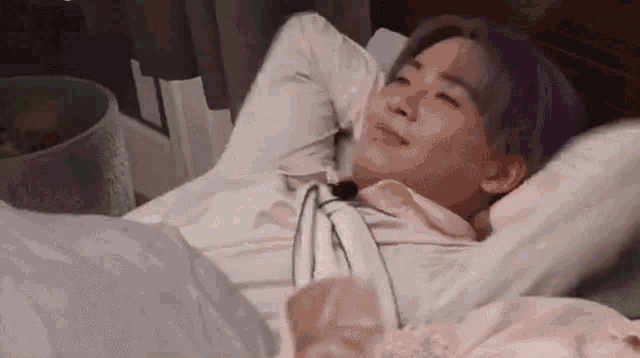 a young man with purple hair is laying in a bed with his arms outstretched .