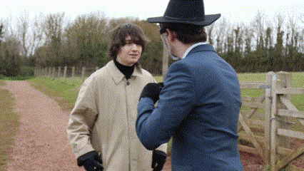 a man in a cowboy hat talks to another man on a dirt road