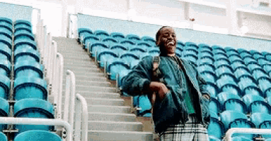 a man in a plaid skirt is standing in a stadium with rows of blue seats