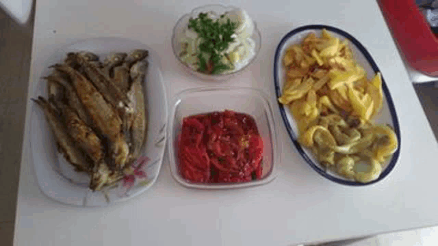 a table topped with plates of food including fried fish , tomatoes , and peppers .