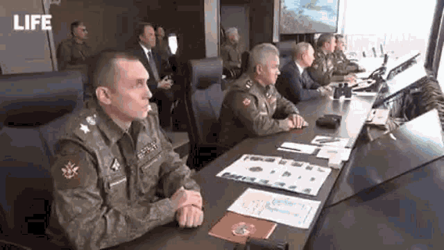 a group of men in military uniforms are sitting at a long table .