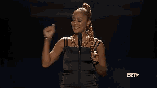 a woman in a black dress stands in front of a microphone with the bet logo in the background