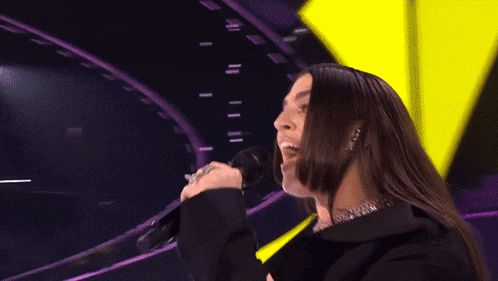 a woman with long hair singing into a microphone with a yellow and purple background