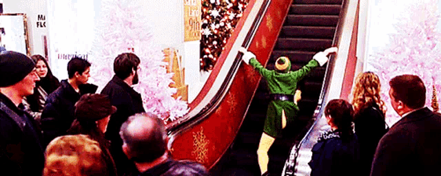 a man in a green elf costume is riding an escalator in a mall