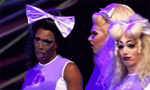 a group of drag queens are standing next to each other in purple outfits .