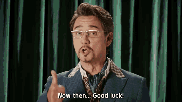 a man wearing glasses and a suit says now then good luck
