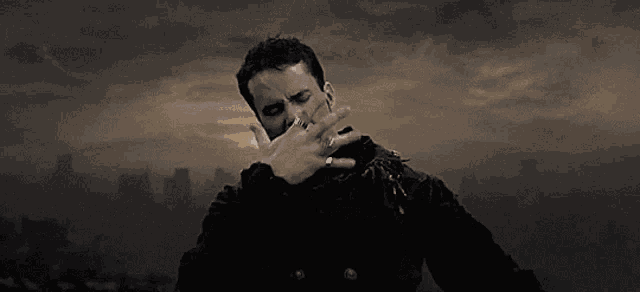 a man in a black jacket is singing in front of a city skyline