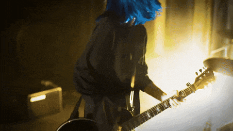 a person with blue hair playing a guitar in a dark room