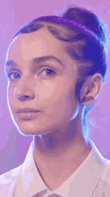 a close up of a woman 's face with her hair in a bun and a purple background .