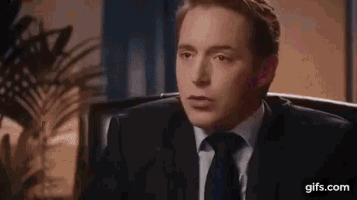 a man in a suit and tie is sitting in a chair looking at the camera .