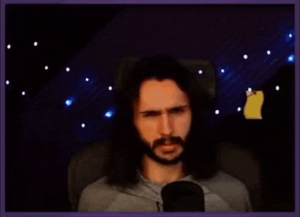 a man with long hair and a beard is sitting in front of a microphone making a funny face .