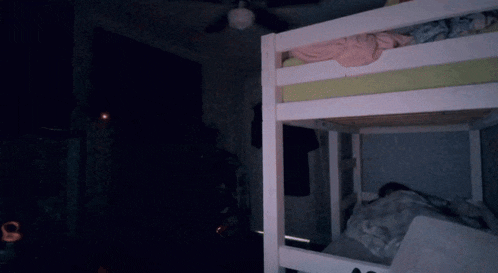 a man in a white tank top stands in a dark room next to a bunk bed