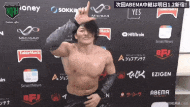 a shirtless wrestler stands in front of a wall that says abema live on it