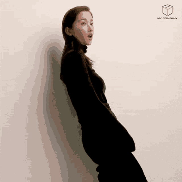 a woman in a black turtleneck is standing in front of a white wall with my company written on it