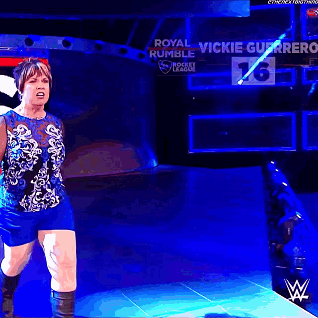 a woman in a blue top and shorts stands in front of a sign that says royal rumble
