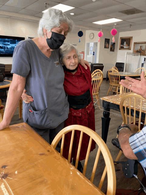 a woman wearing a mask is hugging another woman