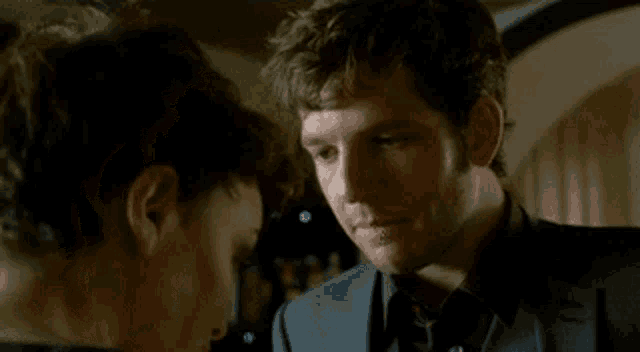 a man in a suit and tie is looking at another man in a black shirt .