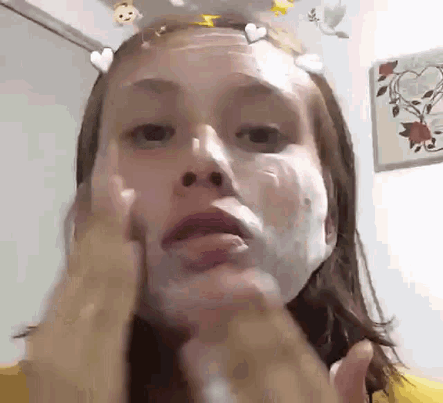 a woman is applying a mask to her face with hearts on her head