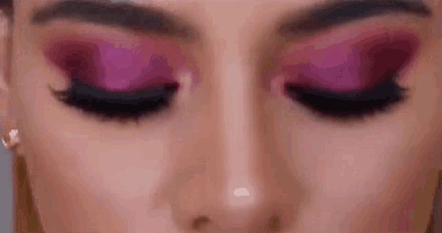 a close up of a woman 's eyes with pink eyeshadow and black eyelashes .