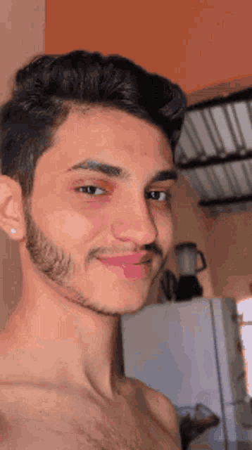a shirtless young man with a beard is taking a selfie in a kitchen