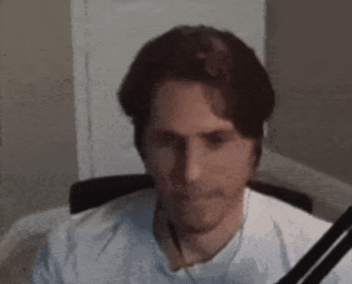 a man in a white shirt is sitting in a chair with a microphone in front of him .